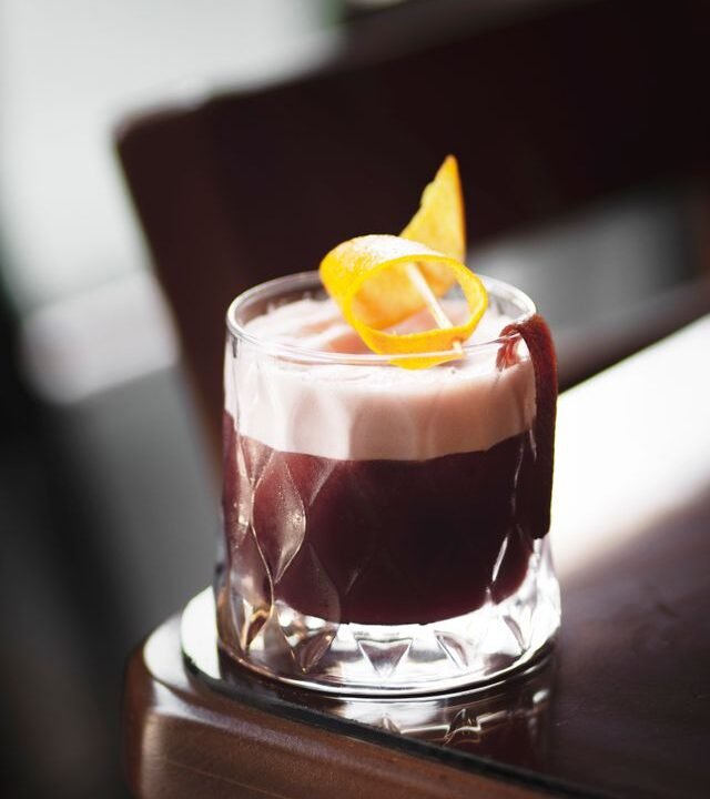 A sophisticated cocktail featuring a foam layer and orange twist garnish, perfect for upscale settings.
